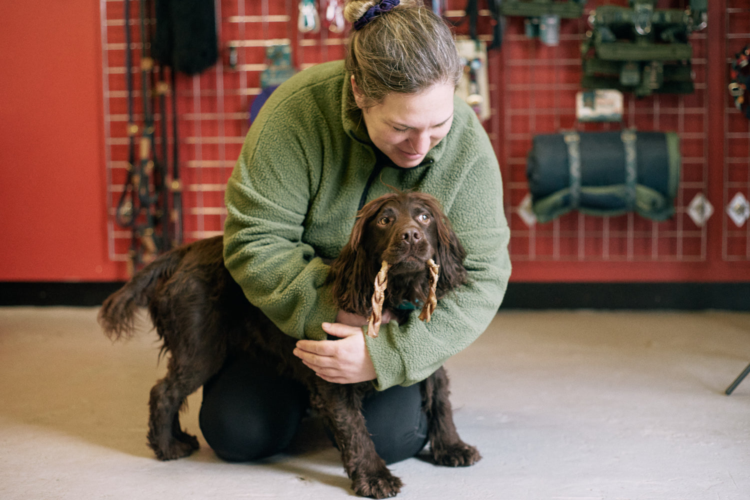 Amy from Track and Trail Canine Outfitters hugging Max, her rescue cocker spaniel who has a chewed camel braid in his mouth.
