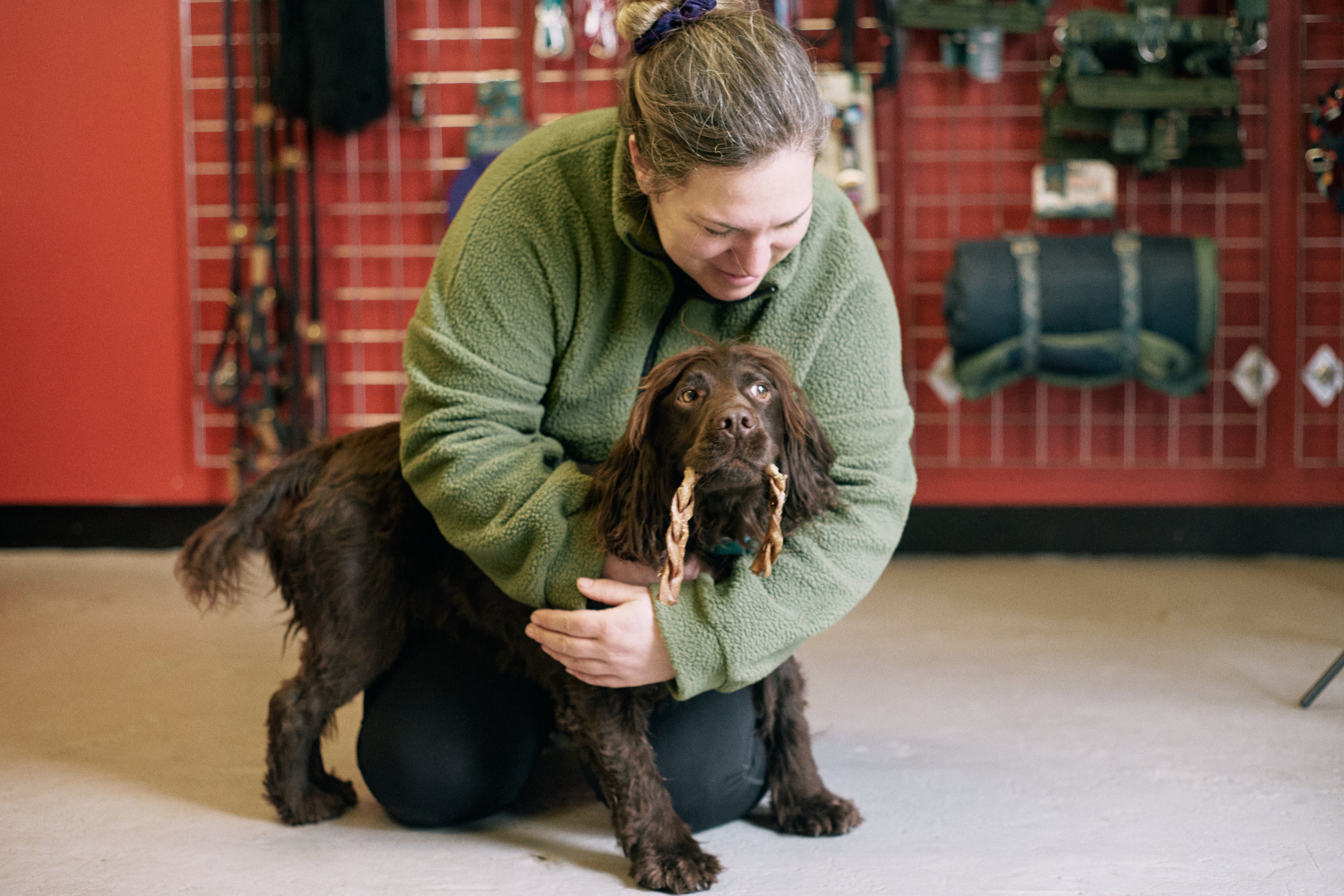 Amy from Track and Trail Canine Outfitters hugging Max, her rescue cocker spaniel who has a chewed camel braid in his mouth.